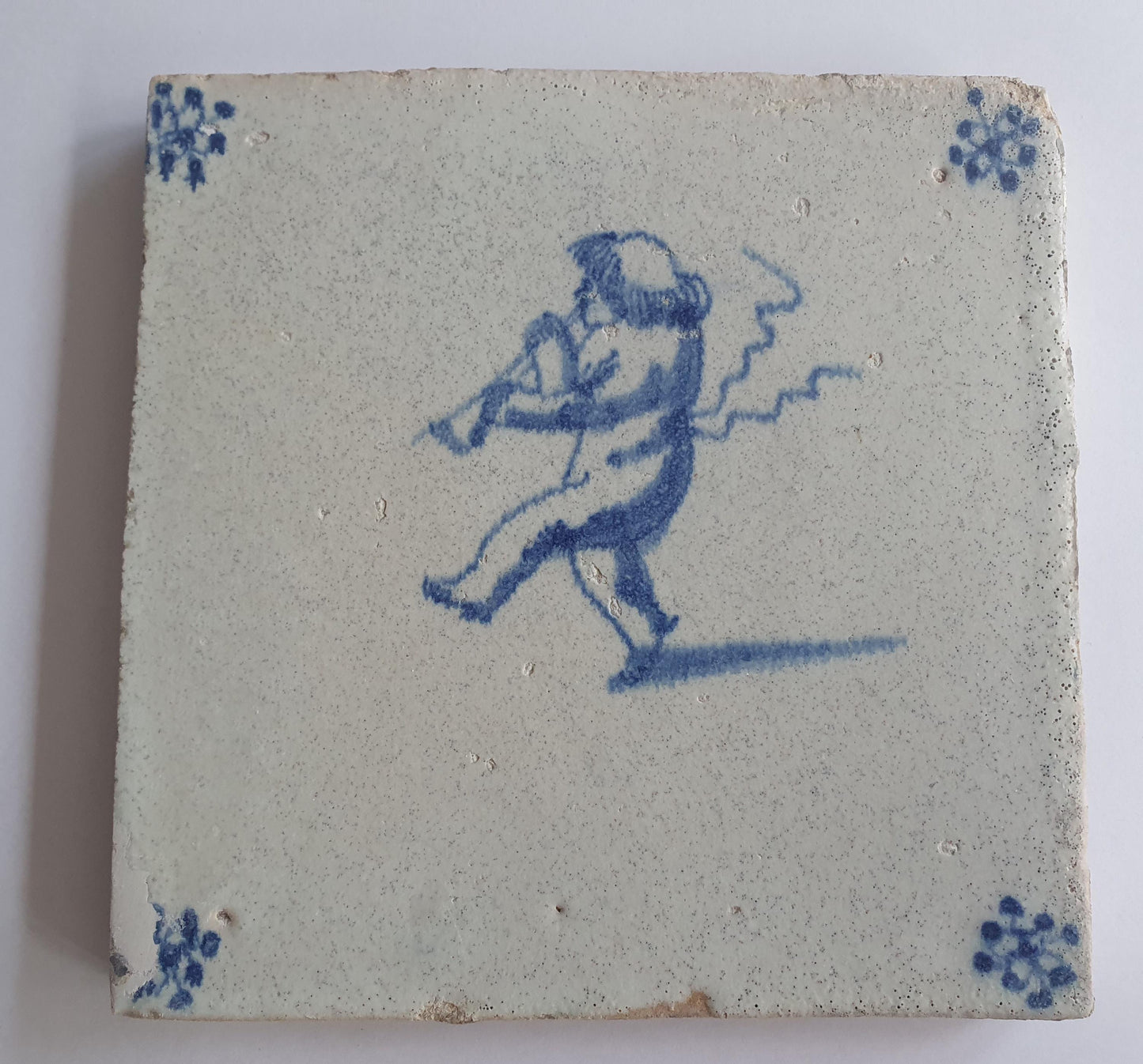 This antique Delft tile, dating from around 1660, depicts Cupid blowing a trumpet.