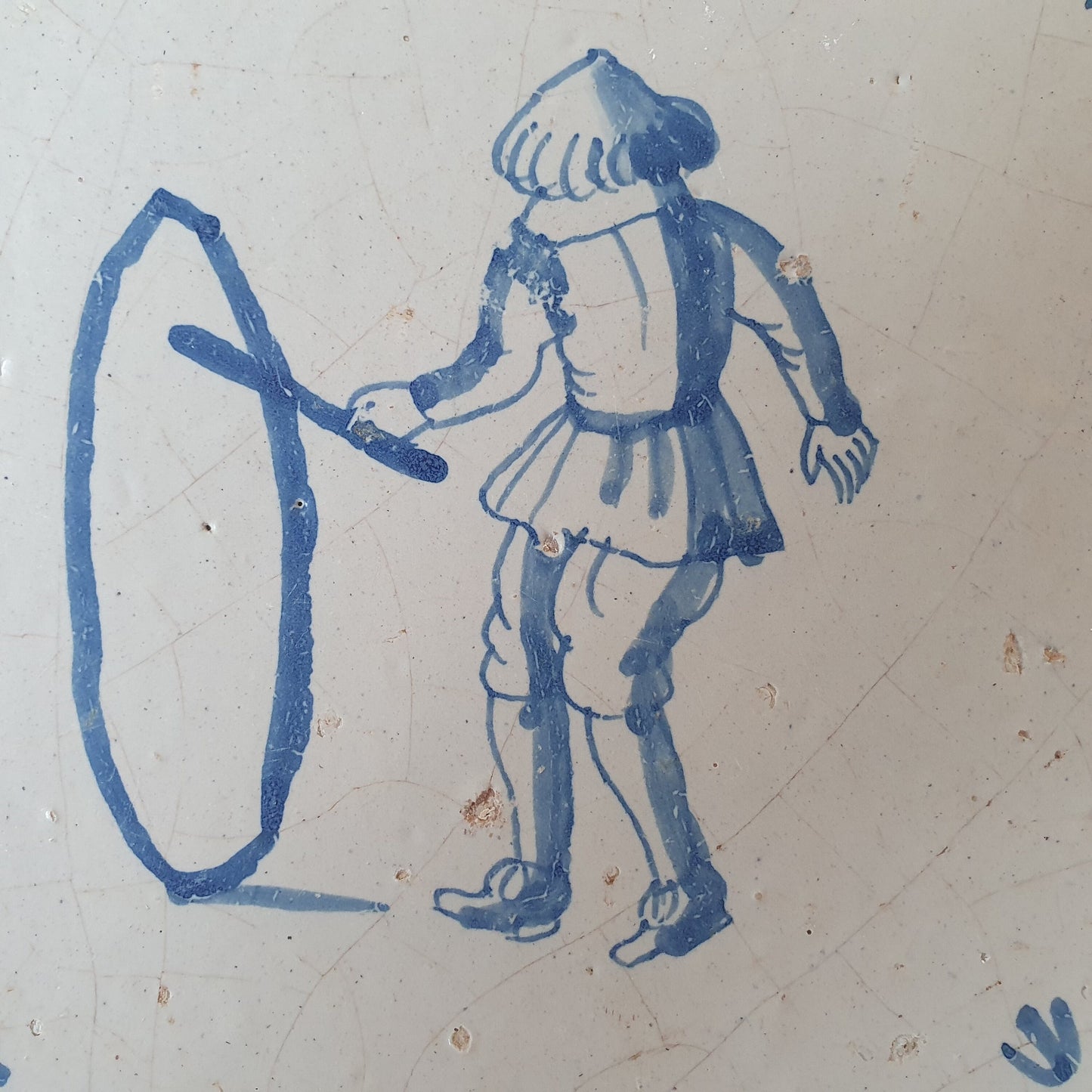 Nederlands antiek - tegel jongen met hoepel, kinderspel , gedecoreerd met een ossenkop hoekmotief - gedateerd  1640