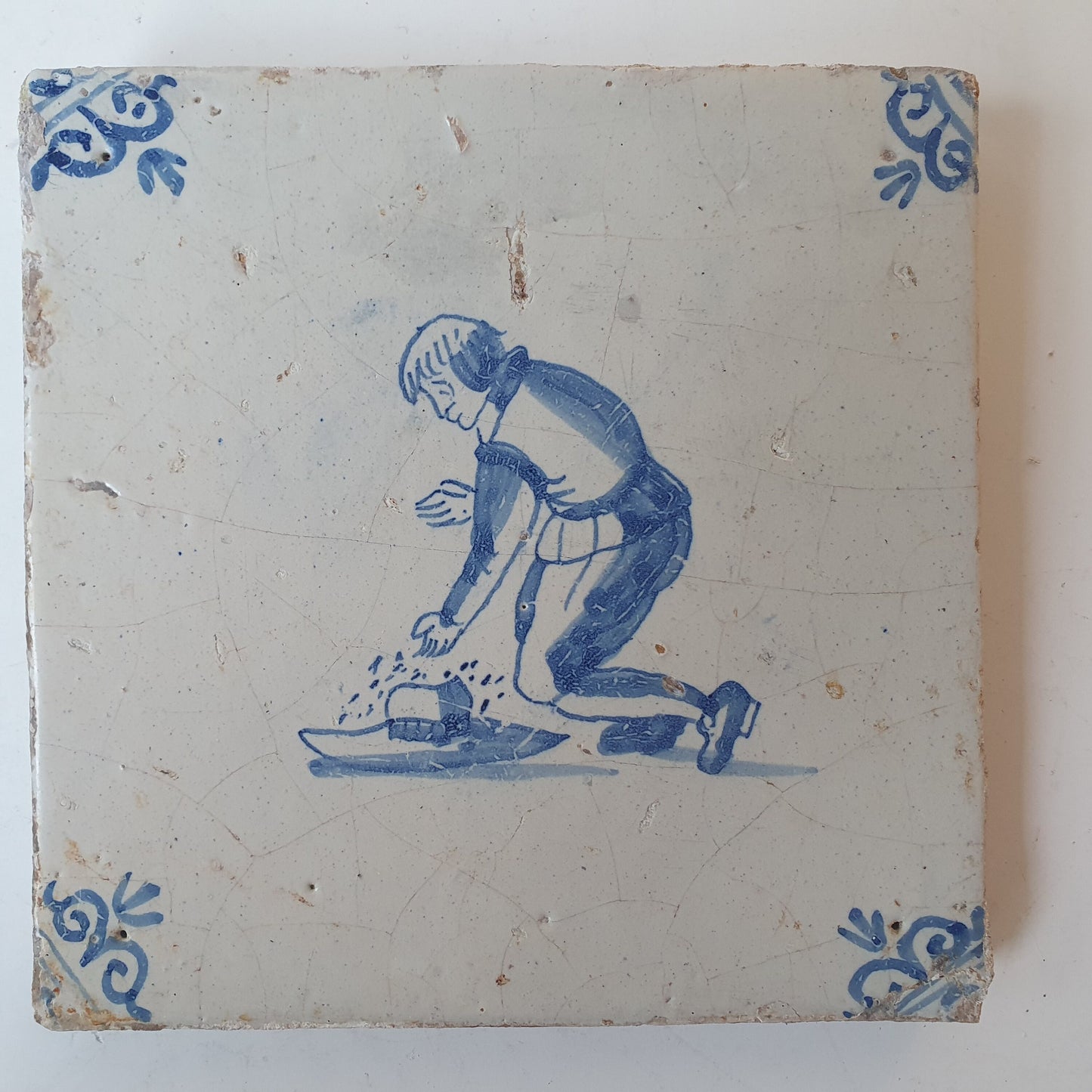 Nederlands antiek - tegel jongen met hoed, kinderspel , gedecoreerd met een ossenkop hoekmotief - gedateerd  1640
