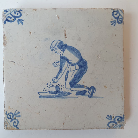 Nederlands antiek - tegel jongen met hoed, kinderspel , gedecoreerd met een ossenkop hoekmotief - gedateerd  1640