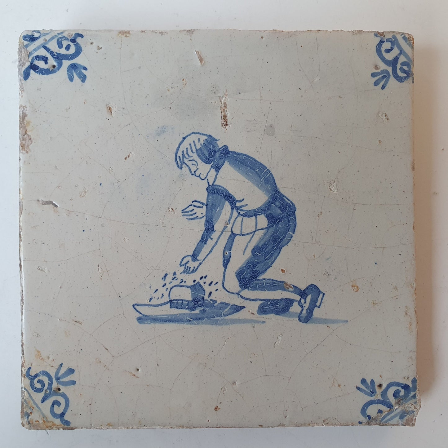 Nederlands antiek - tegel jongen met hoed, kinderspel , gedecoreerd met een ossenkop hoekmotief - gedateerd  1640