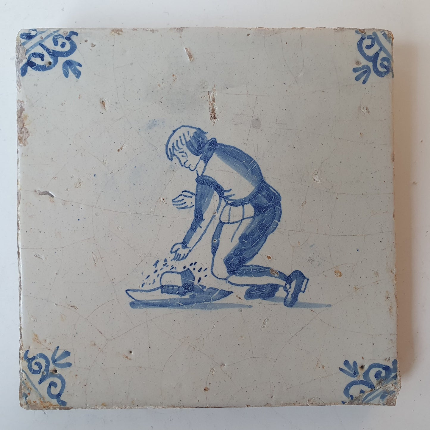 Nederlands antiek - tegel jongen met hoed, kinderspel , gedecoreerd met een ossenkop hoekmotief - gedateerd  1640