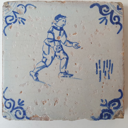Nederlands antiek - tegel :kinderspel , gedecoreerd met een ossenkop hoekmotief - gedateerd  1640