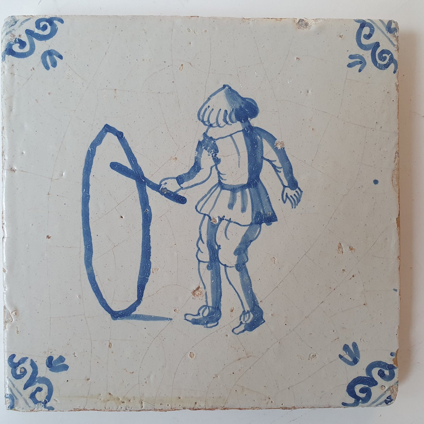 Nederlands antiek - tegel jongen met hoepel, kinderspel , gedecoreerd met een ossenkop hoekmotief - gedateerd  1640