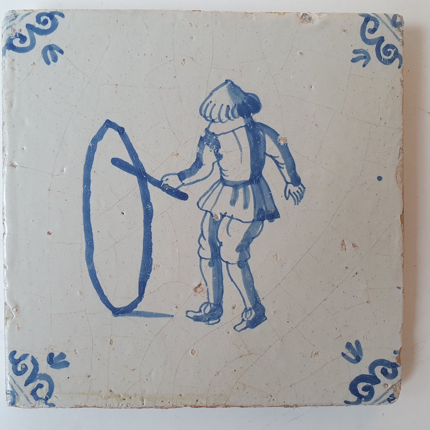 Nederlands antiek - tegel jongen met hoepel, kinderspel , gedecoreerd met een ossenkop hoekmotief - gedateerd  1640