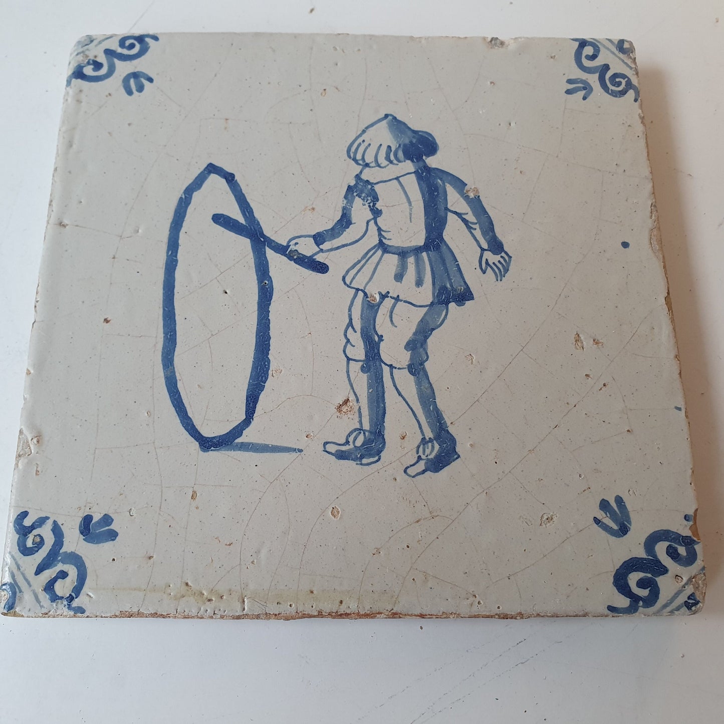Nederlands antiek - tegel jongen met hoepel, kinderspel , gedecoreerd met een ossenkop hoekmotief - gedateerd  1640