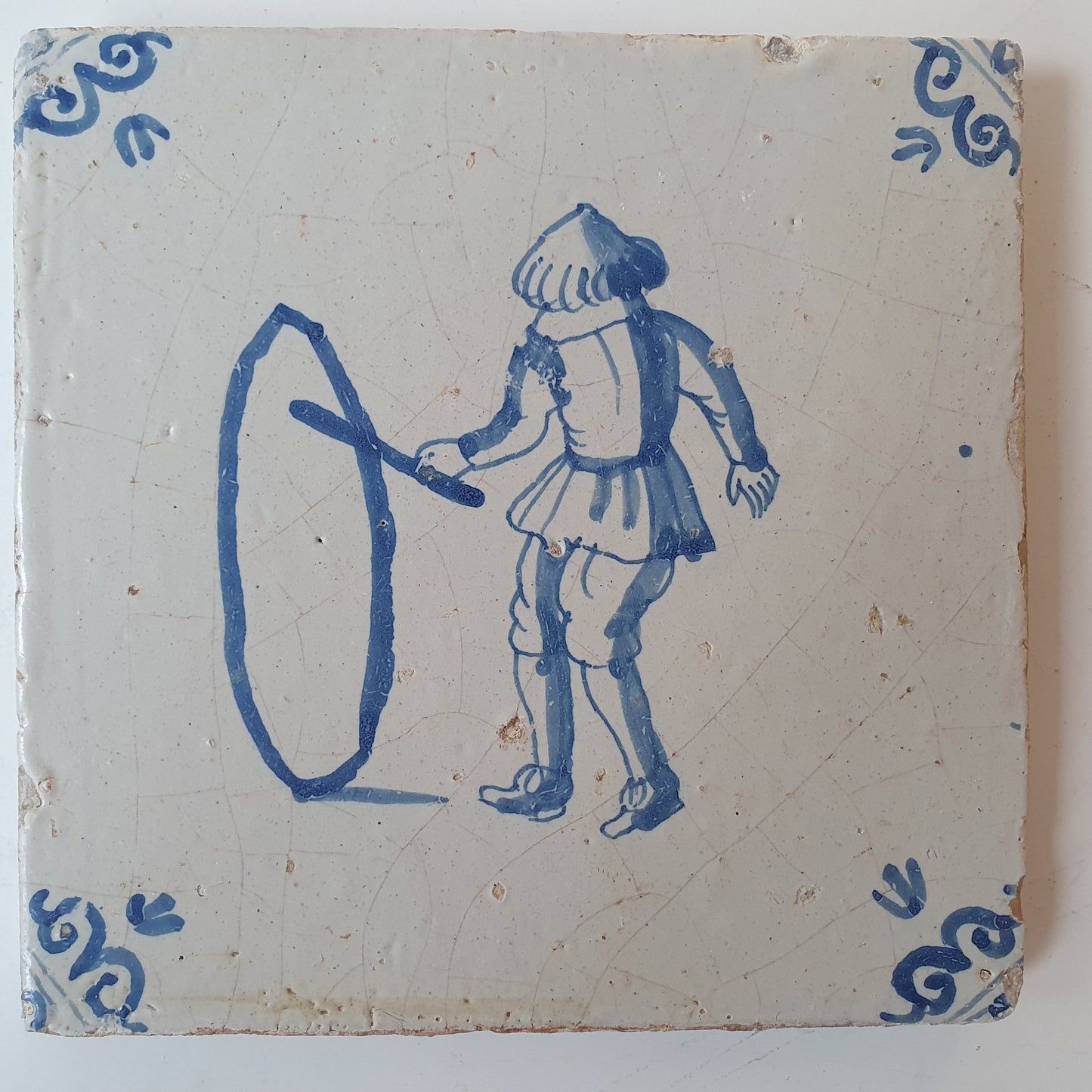 Nederlands antiek - tegel jongen met hoepel, kinderspel , gedecoreerd met een ossenkop hoekmotief - gedateerd  1640