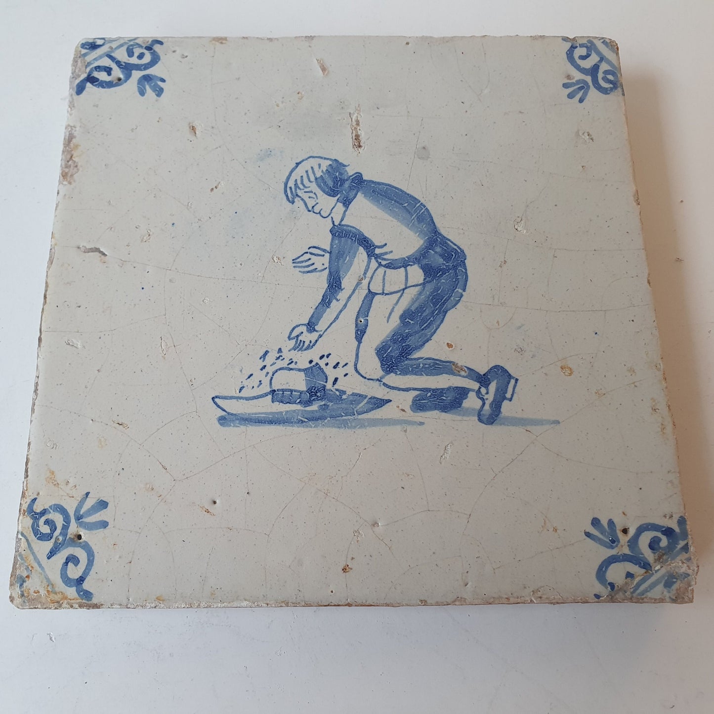 Nederlands antiek - tegel jongen met hoed, kinderspel , gedecoreerd met een ossenkop hoekmotief - gedateerd  1640