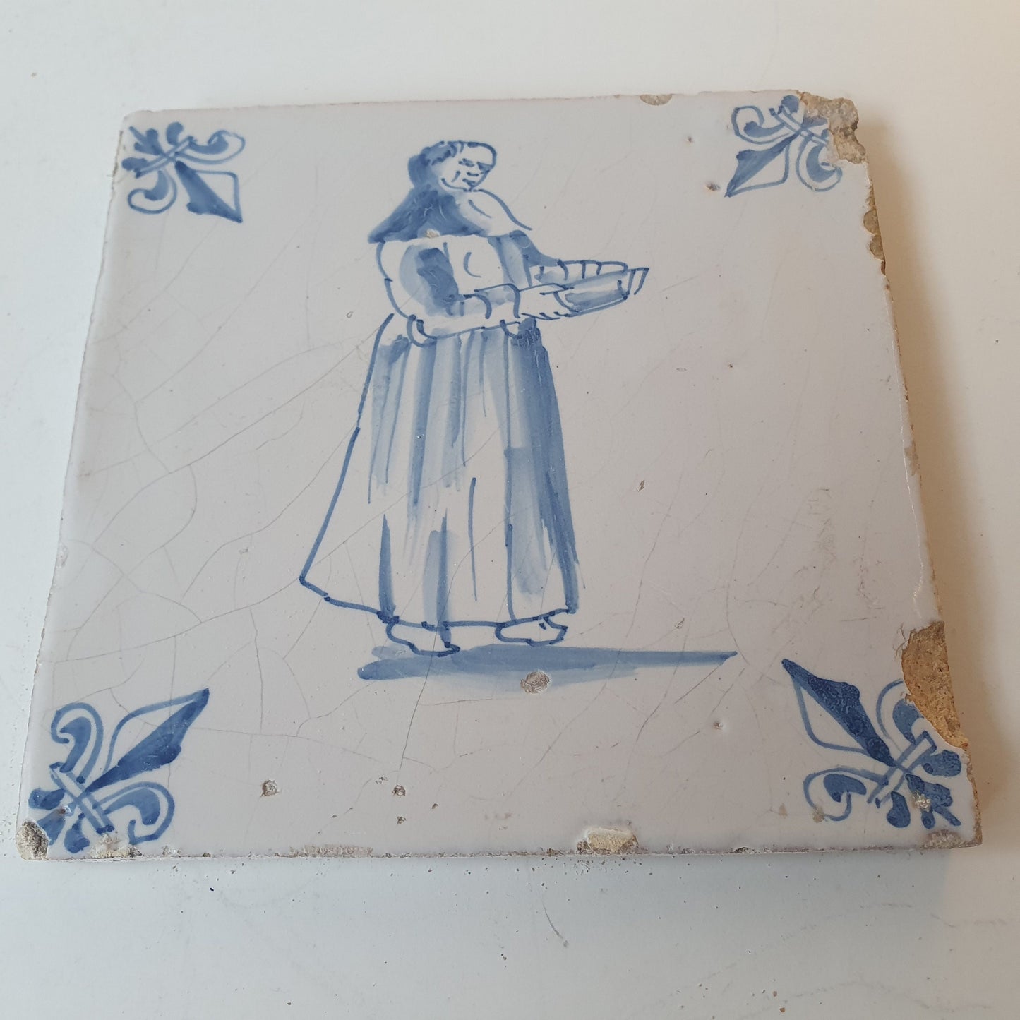 Nederlands antiek - tegel marktkoopvrouw , gedecoreerd met een lelie hoekmotief - gedateerd  1640