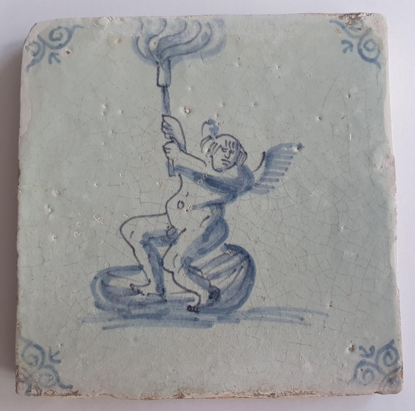 This antique Delft tile depicts Cupid lifting a burning torch in the sky. 17th century