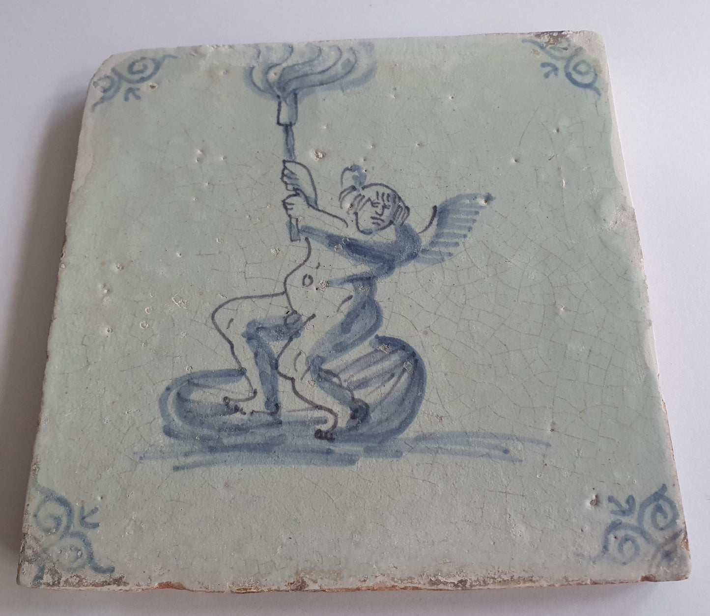 This antique Delft tile depicts Cupid lifting a burning torch in the sky. 17th century