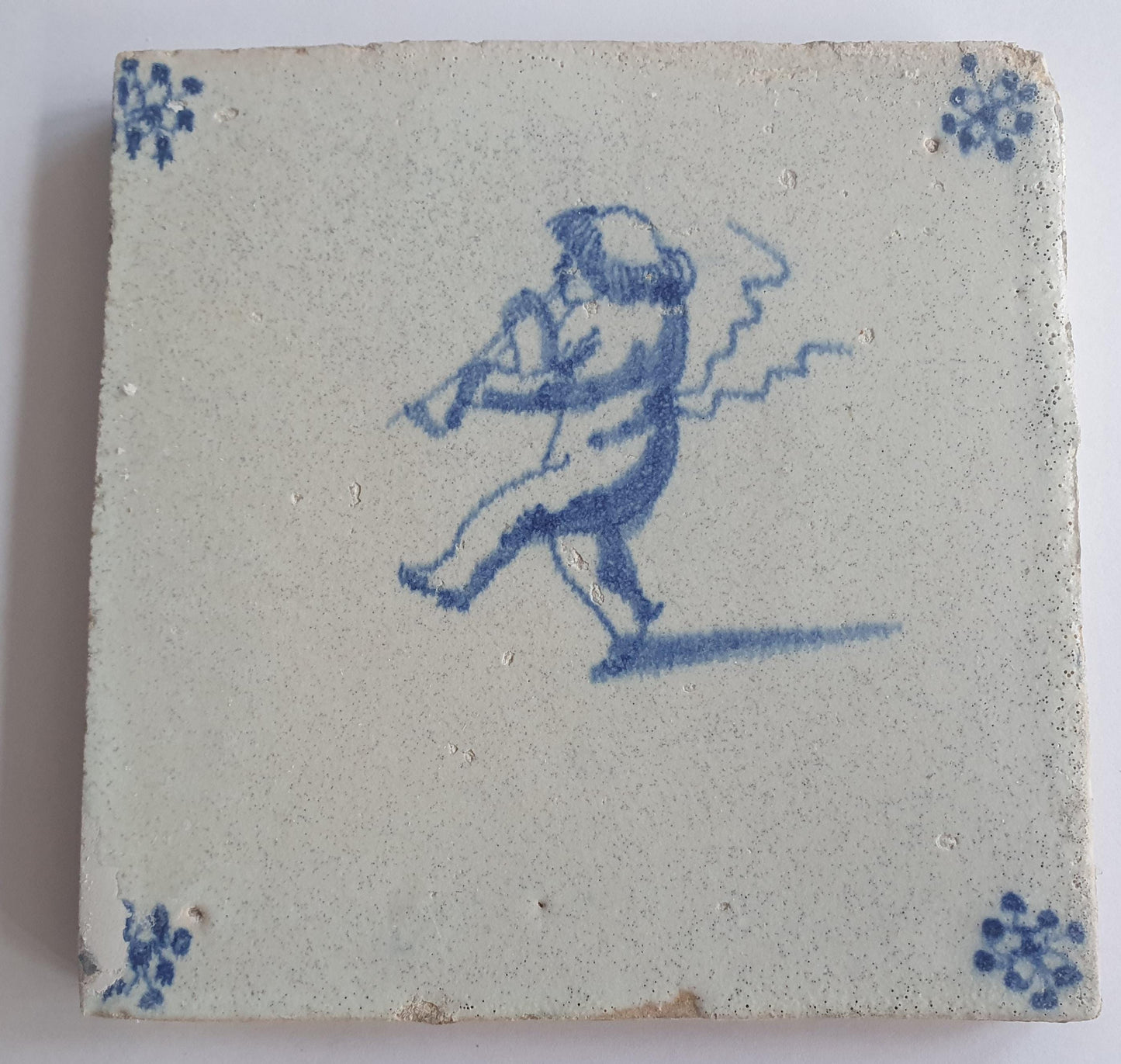 This antique Delft tile, dating from around 1660, depicts Cupid blowing a trumpet.