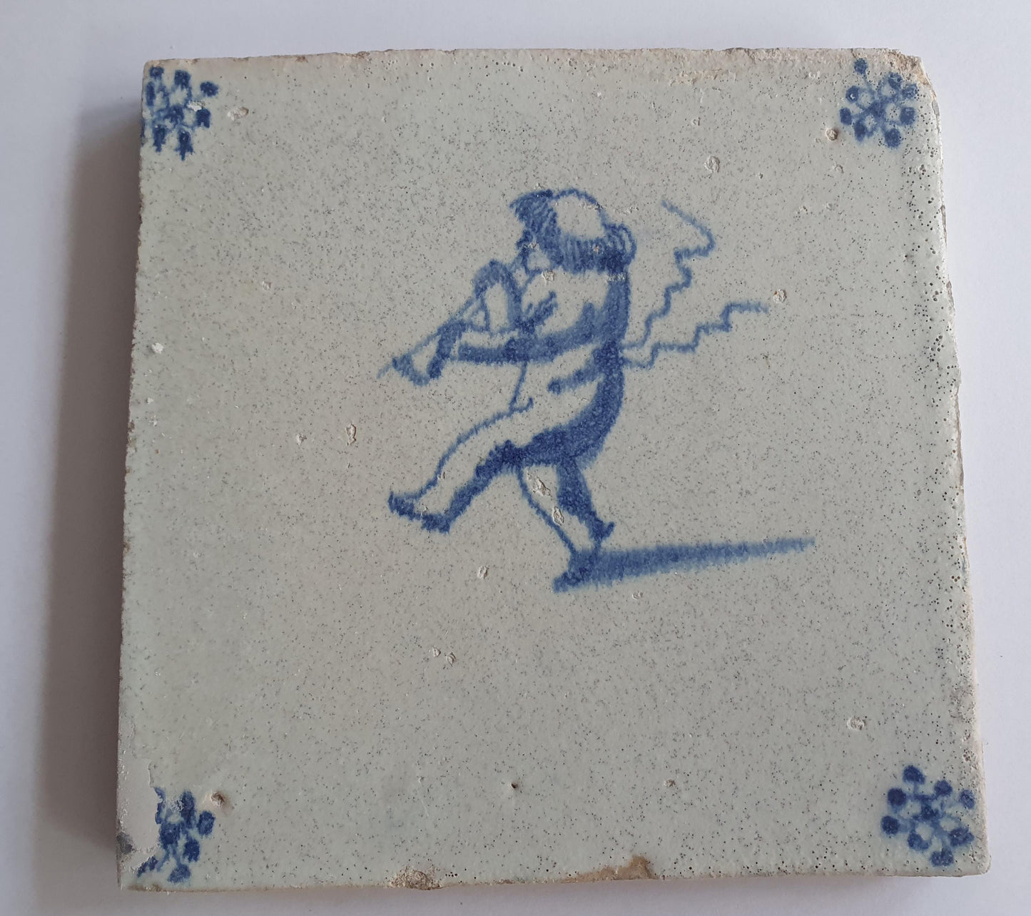 This antique Delft tile, dating from around 1660, depicts Cupid blowing a trumpet.