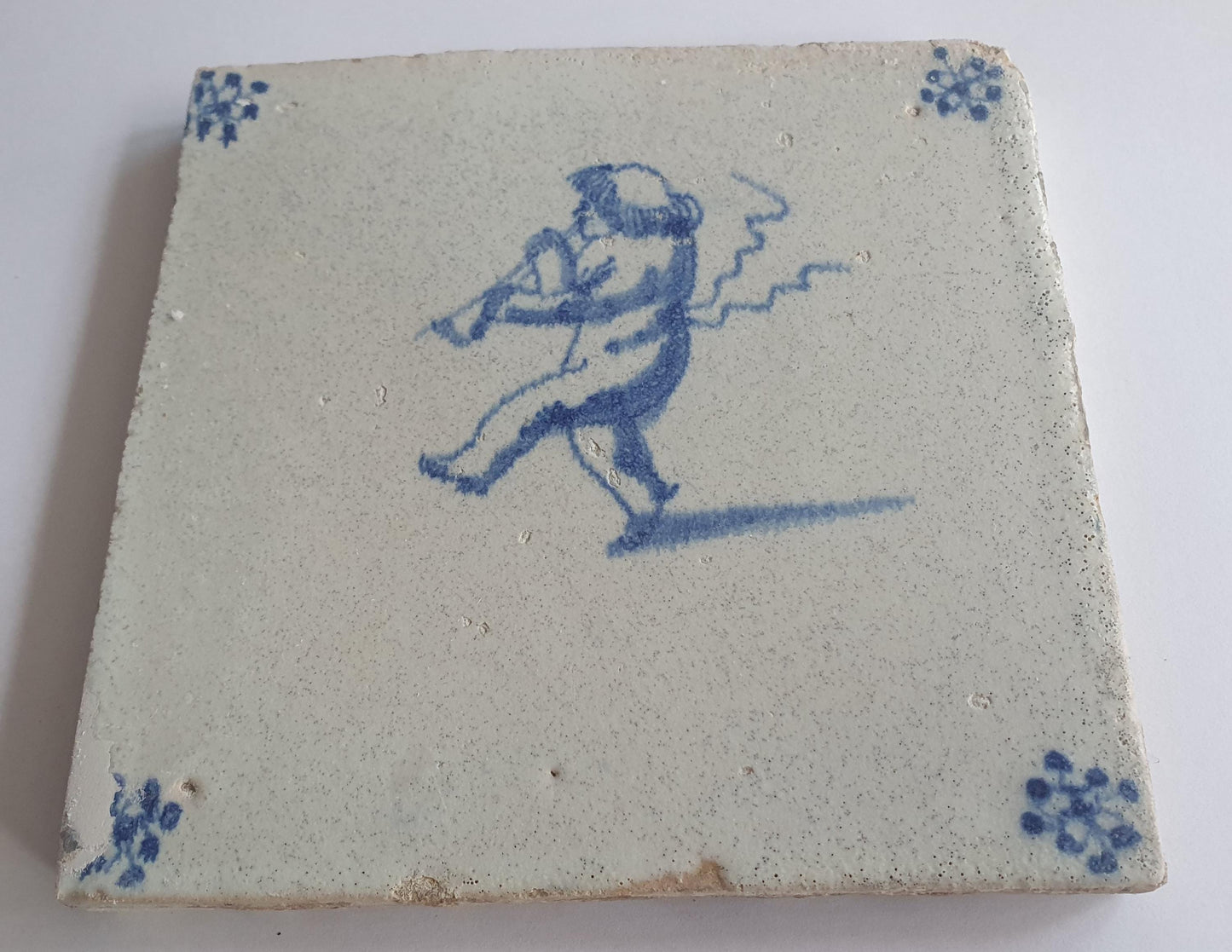 This antique Delft tile, dating from around 1660, depicts Cupid blowing a trumpet.