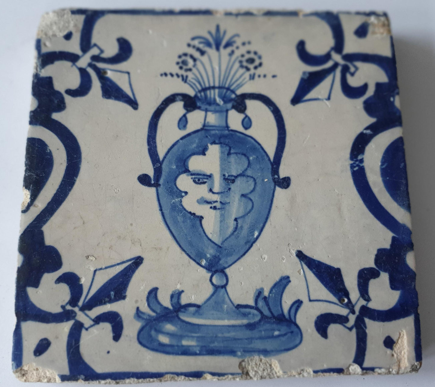 This rare antique Delft tile depicts a flowerpot in blue with face.     around  1620