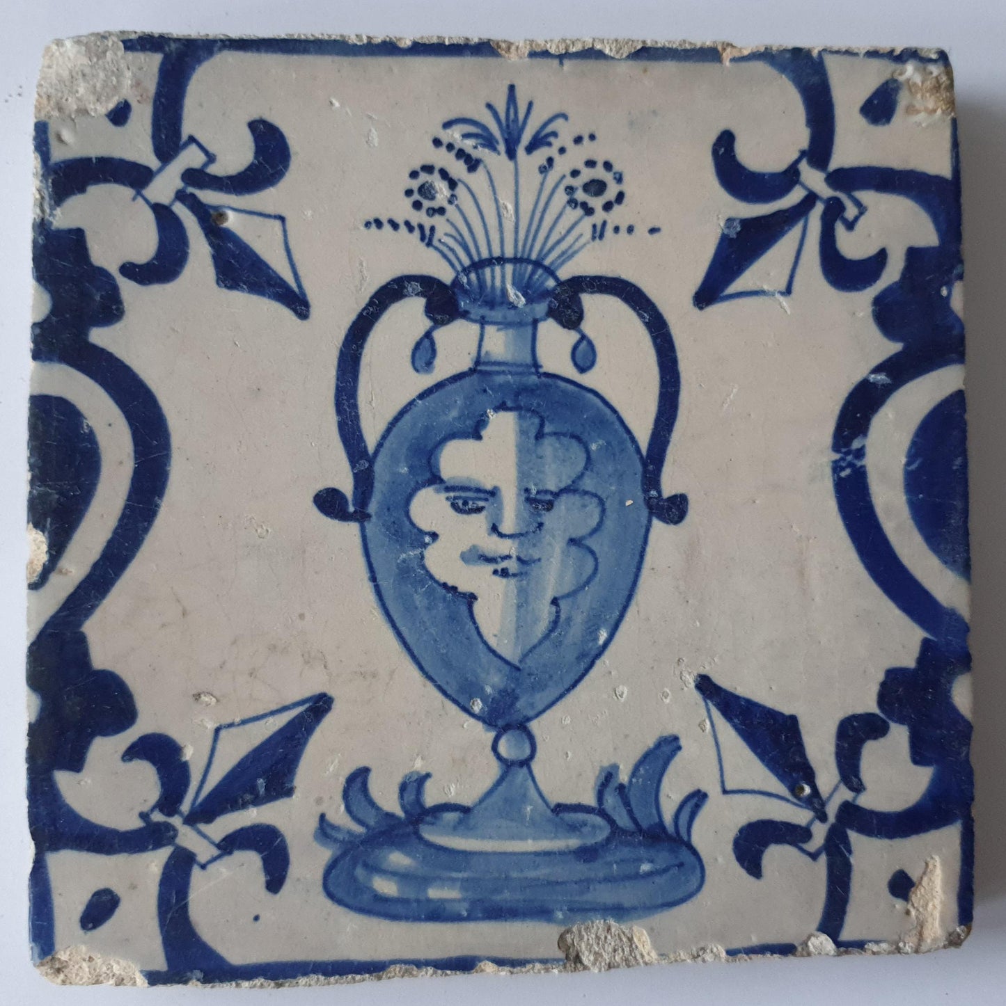 This rare antique Delft tile depicts a flowerpot in blue with face.     around  1620