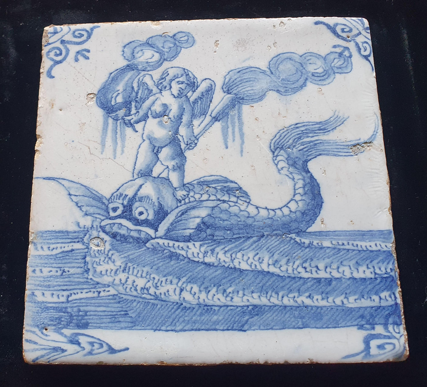 Deze antieke Delftse tegel dateert van rond 1670 en toont een putti op een monsterachtige dolfijn staat, verzameltegel.