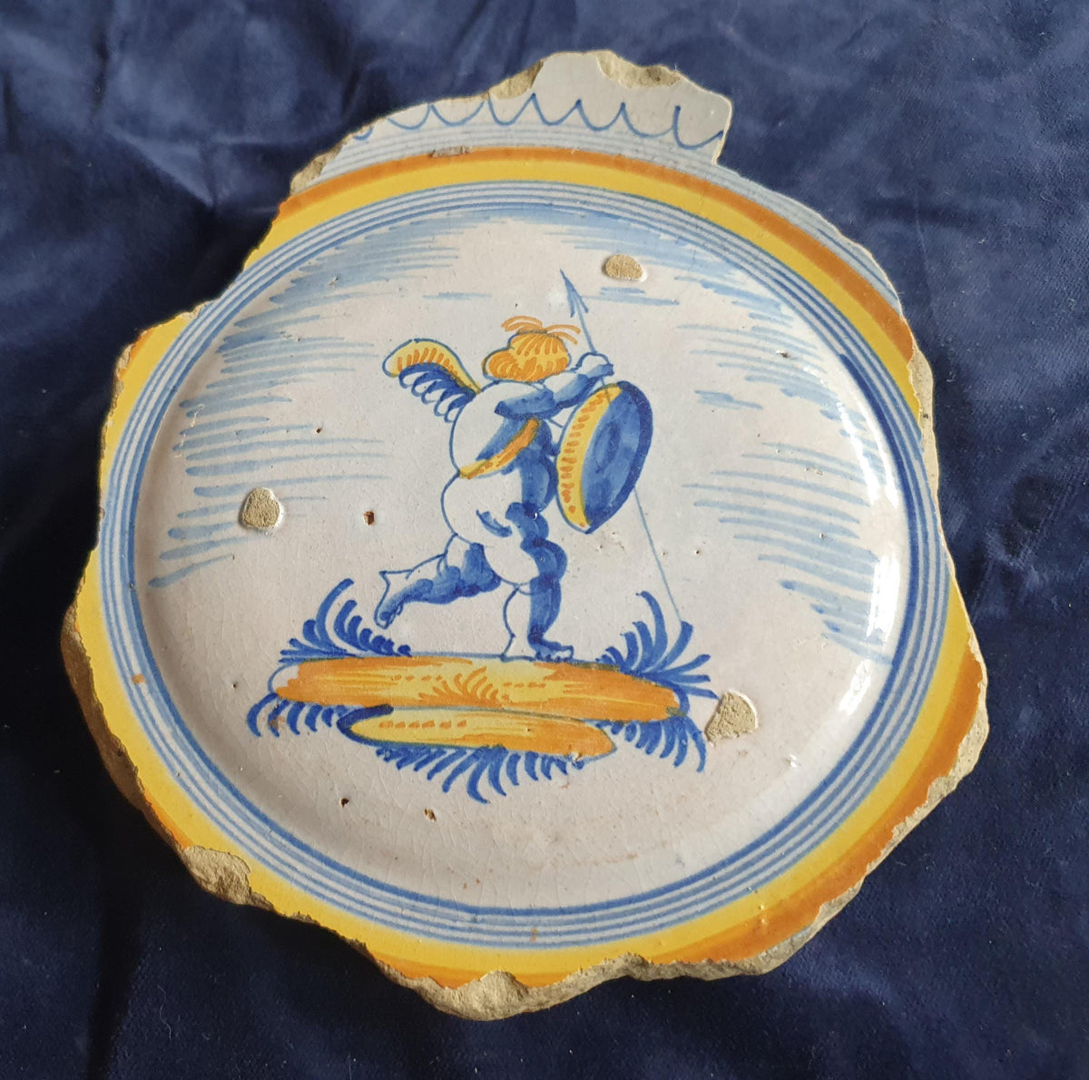 A Large rare majolica fragment depicting a striding putto on base, with spear and shield and a sash draped over the shoulder. 20 x 16 cm.
