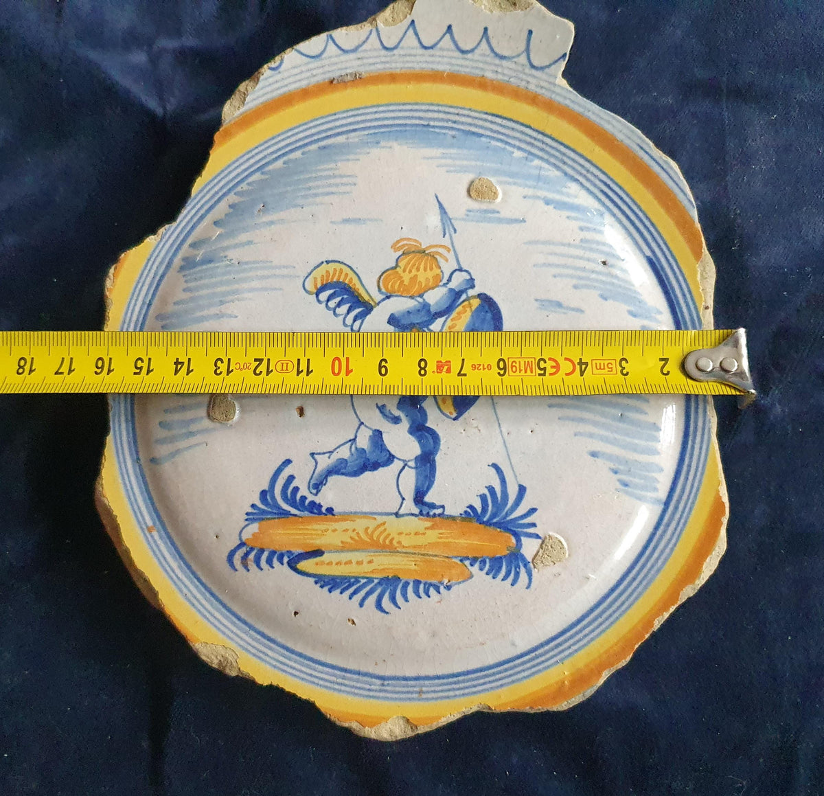 A Large rare majolica fragment depicting a striding putto on base, with spear and shield and a sash draped over the shoulder. 20 x 16 cm.