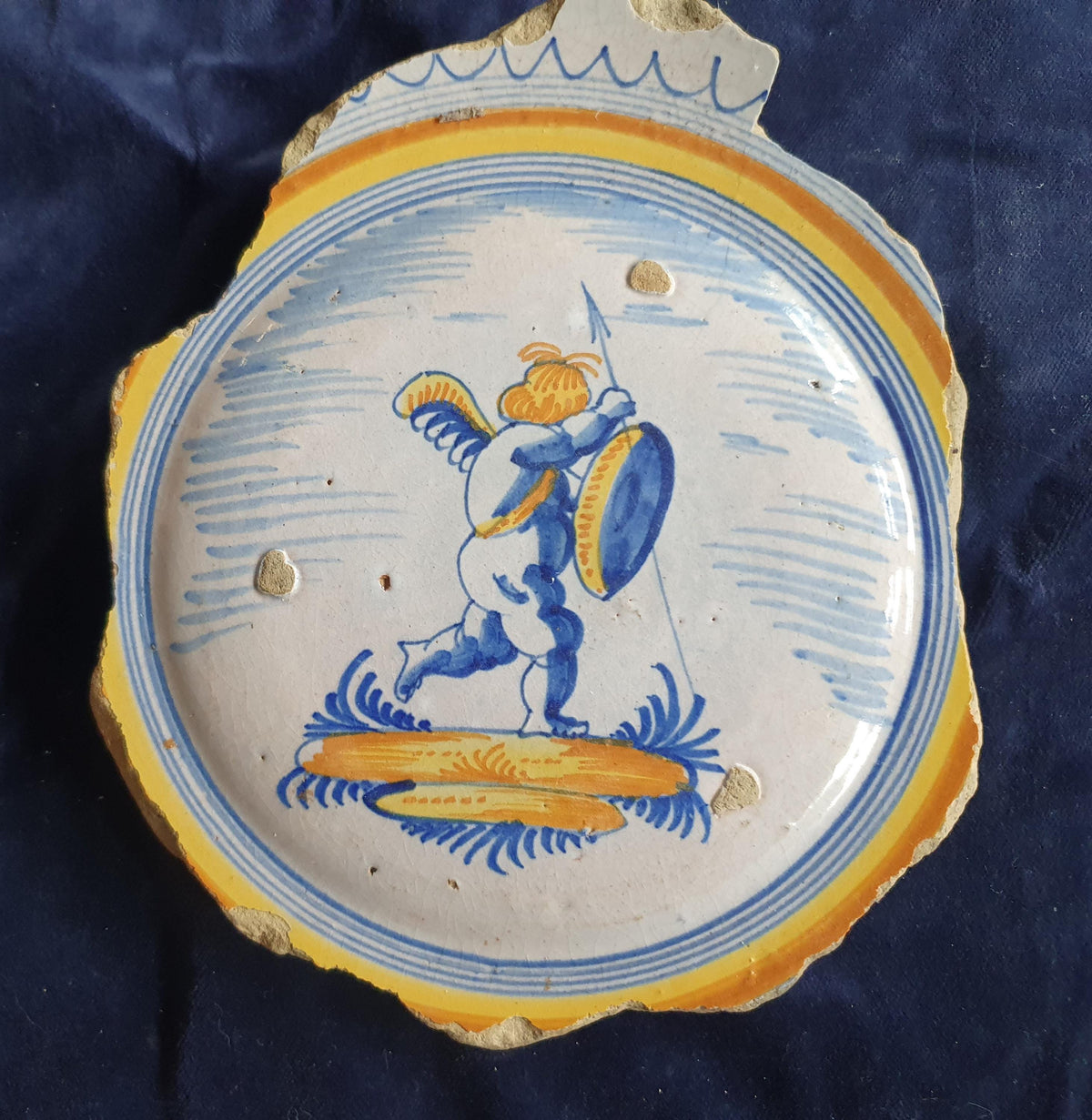 A Large rare majolica fragment depicting a striding putto on base, with spear and shield and a sash draped over the shoulder. 20 x 16 cm.