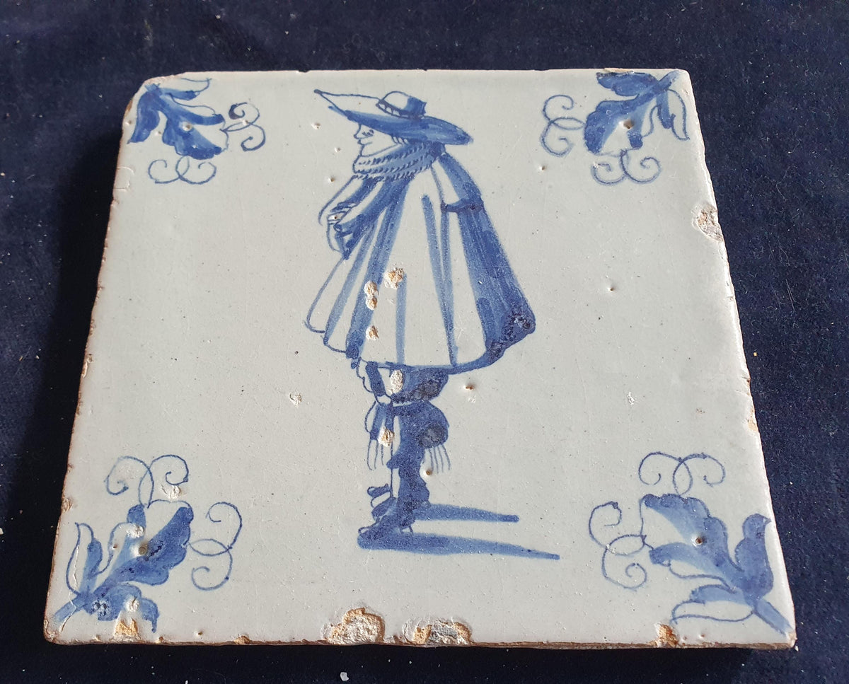 Antique Delft tile depicts a stylishly dressed gentleman in blue; he is wearing a large hat. Figuretile