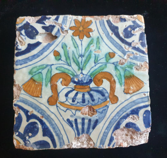 Delft tile from circa 1620 is decorated in polychrome and features a stylized vase containing various stylized flowers. Planttile