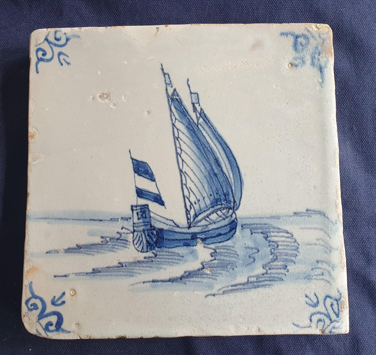 Delft tile, dating from circa 1660, is painted in blue and depicts a ship sailing. Shiptile
