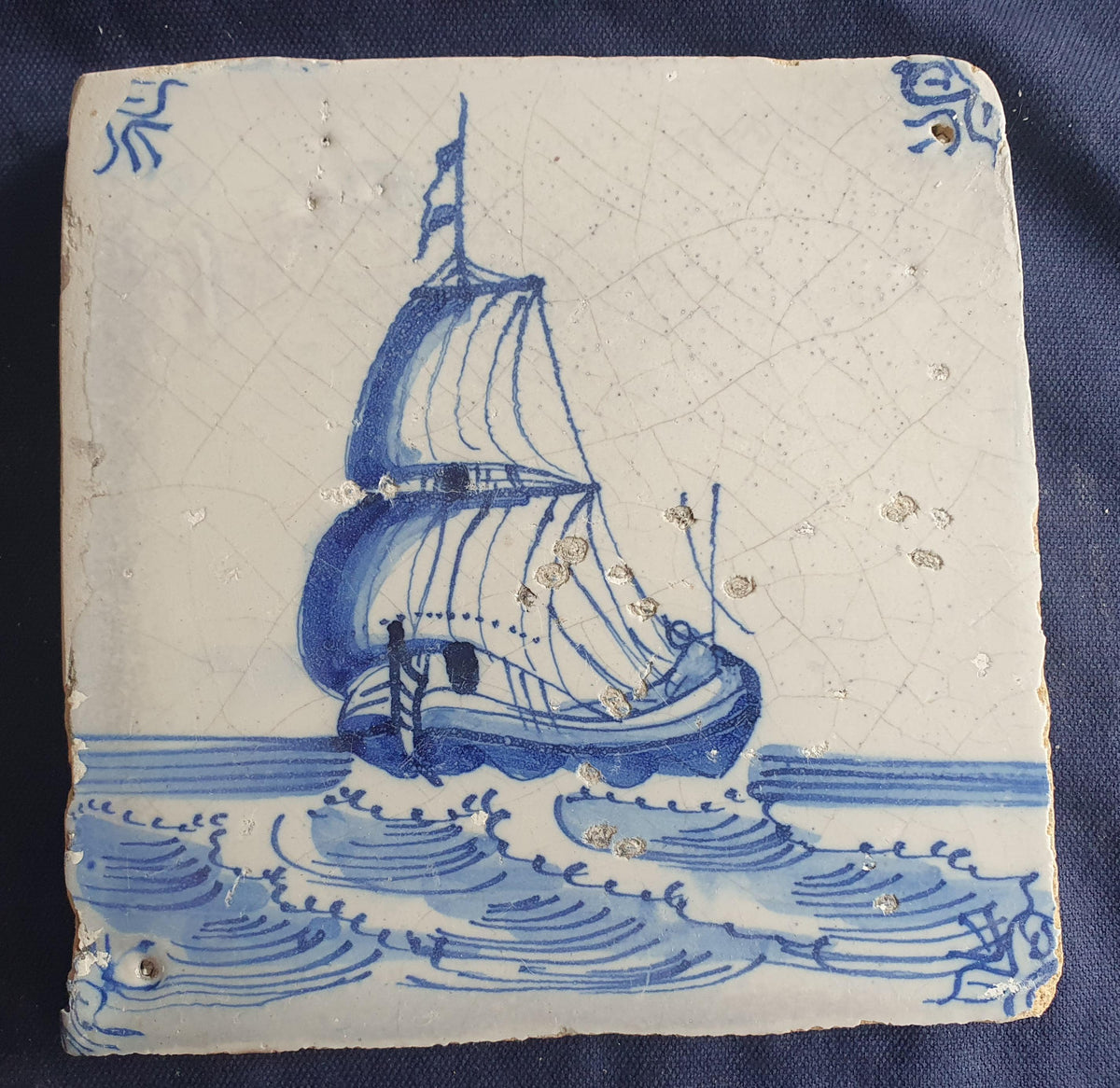 Delft tile, dating from circa 1660, is painted in blue and depicts a ship sailing. Shiptile