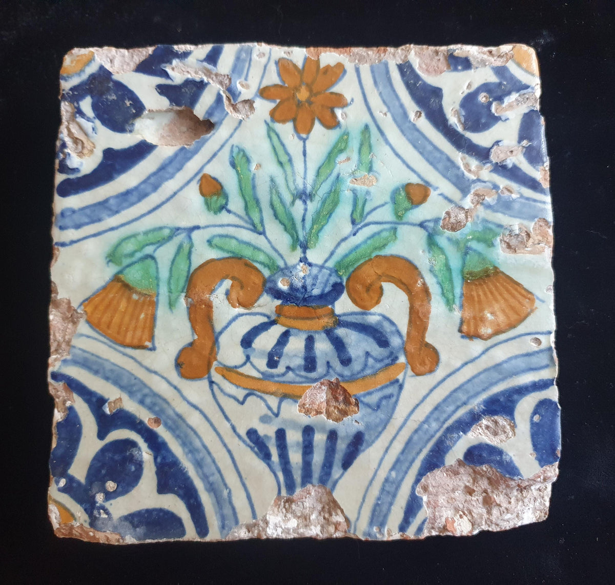 Delft tile from circa 1620 is decorated in polychrome and features a stylized vase containing various stylized flowers. Planttile