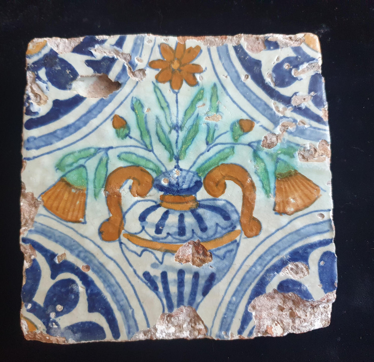 Delft tile from circa 1620 is decorated in polychrome and features a stylized vase containing various stylized flowers. Planttile