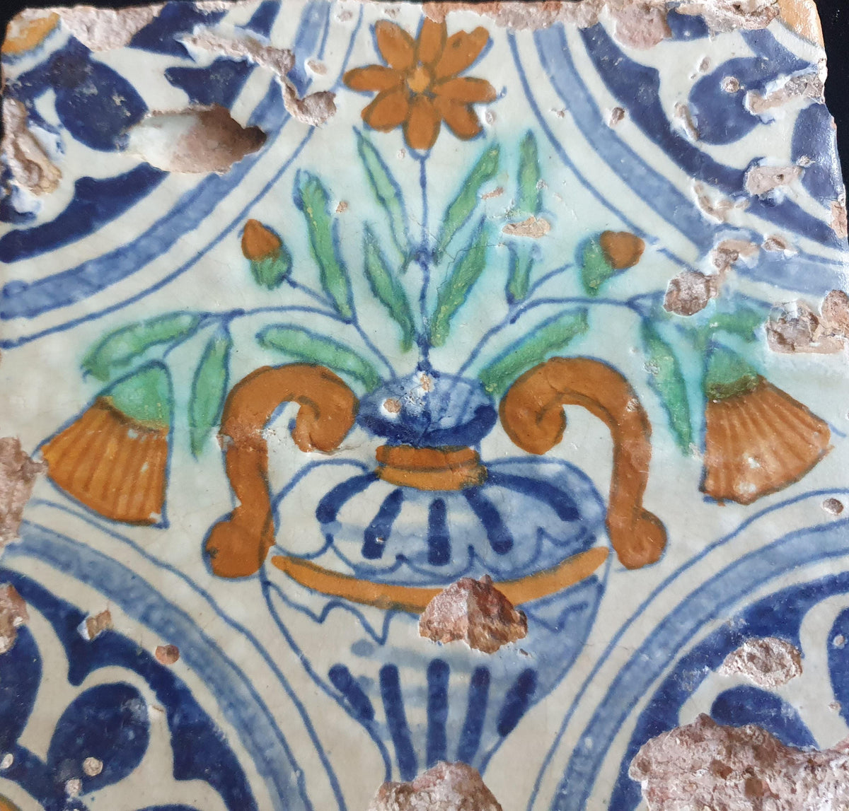 Delft tile from circa 1620 is decorated in polychrome and features a stylized vase containing various stylized flowers. Planttile