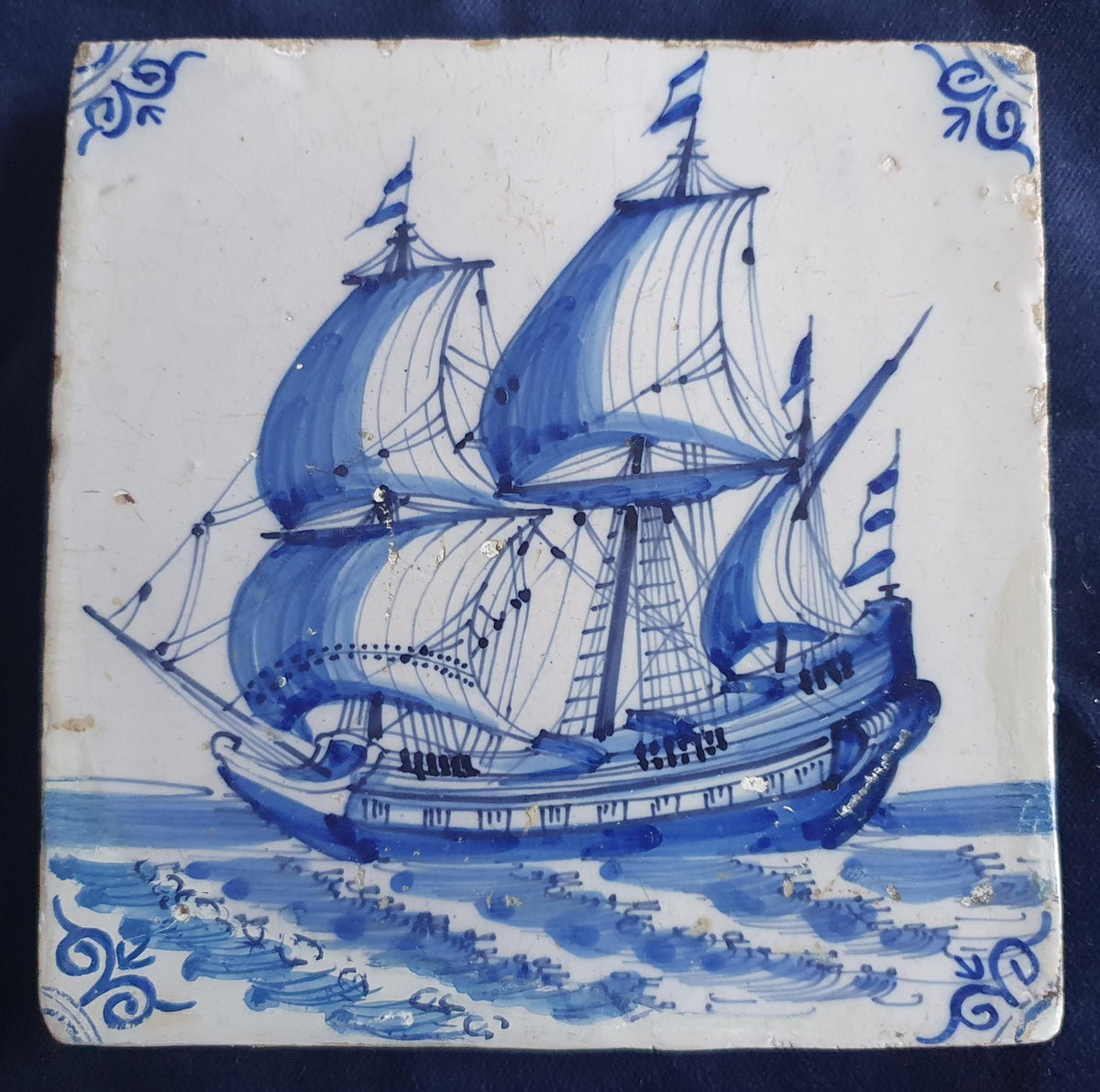 Antique Delft tile dating from around 1650, featuring a beautifully painted depiction of a fully rigged warship at sea. Shiptile